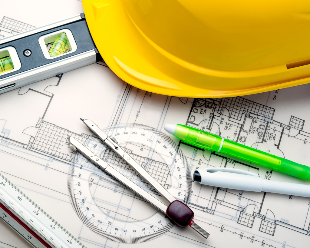 Yellow hardhat sitting on a table with blueprints for a home and a few other tools