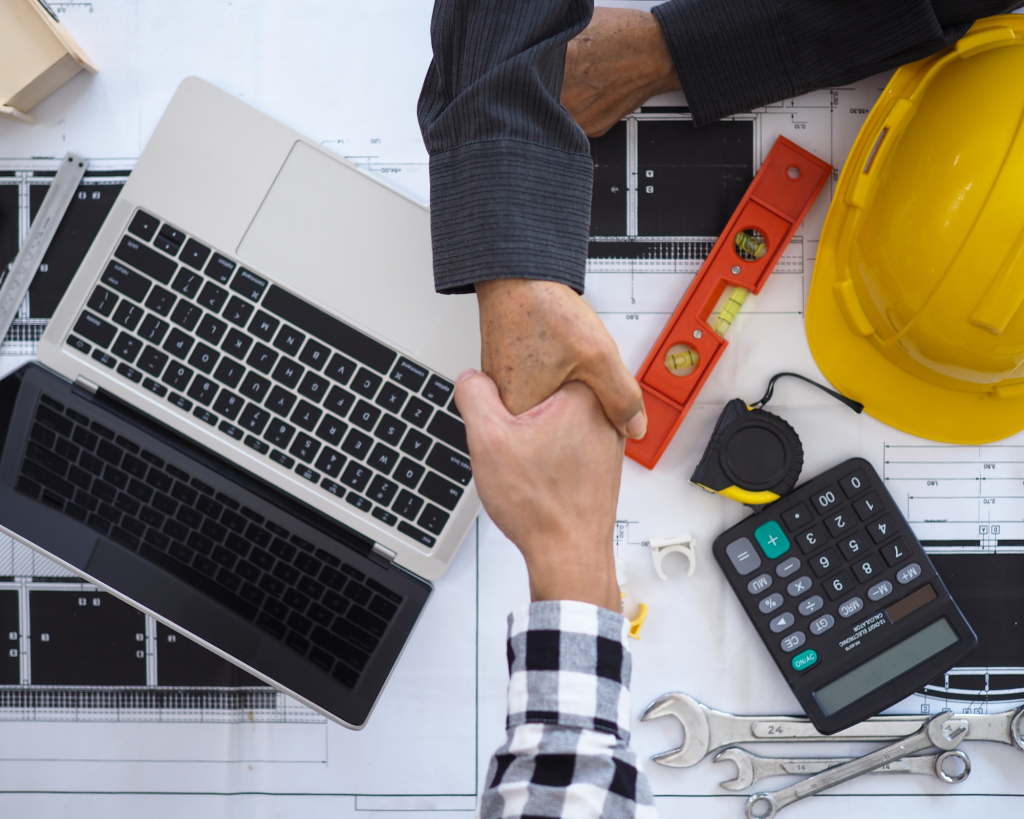 Men shaking hands at a desk over blueprints.