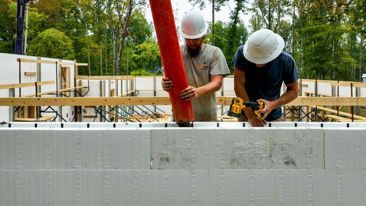 Two men standing on a scaffolding with a hose from a concrete pump truck filling an ICF Form